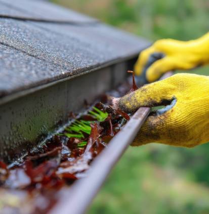 Gloved hand gutter roof leaves debris cleaning worker yellow glove rainwater maintenance